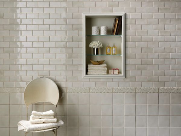 A beautiful white tiled bathroom with a chair and a shelf.