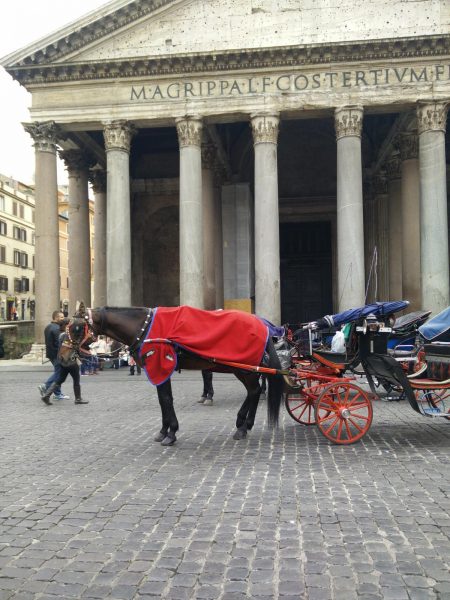 A horse pulling a carriage in front of a building in Rome.