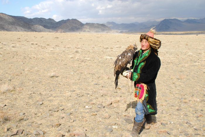 Man in Kazakh clothing with golden eagle in desert