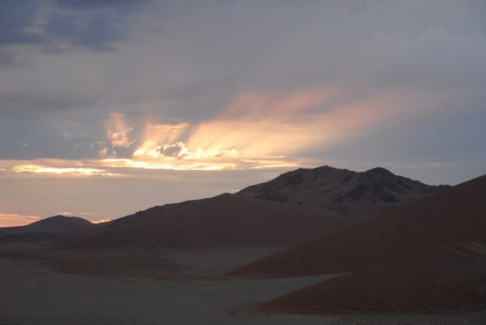 Red sand dunes with sunrise through clouds