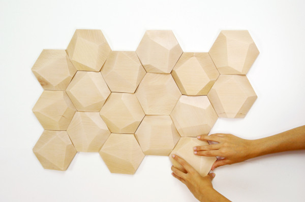 A person is touching a faceted wooden hexagon wall.