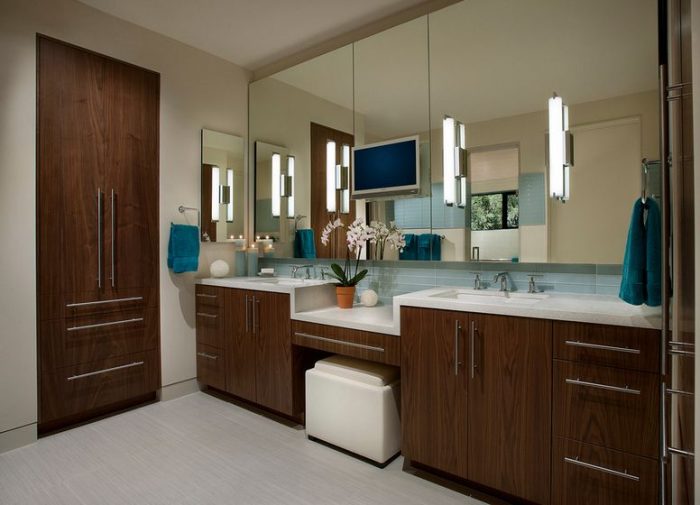 A modern bathroom with wooden cabinets, mirrors, and sconce lighting.