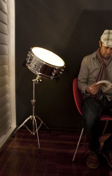 A man reading an upcycled book in front of a drum lamp.