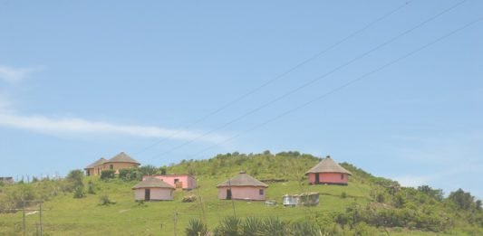 Three rondavels on hill with road and blue sky, South Africa road trip