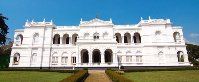 A large white building with arches in the middle of a green lawn in Sri Lanka.