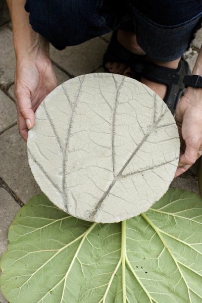A person is holding up a DIY leaf-shaped concrete plate.