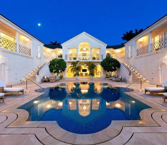 A luxurious white house with a pool at night.