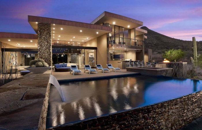A luxurious modern home with a pool and lounge area at dusk.