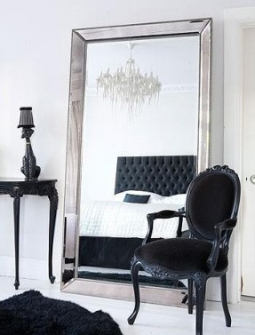 A windowless black and white bedroom with a large mirror.