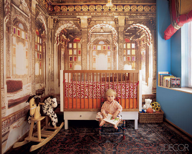 A child is sitting on a rocking chair in a child’s room with a mural.