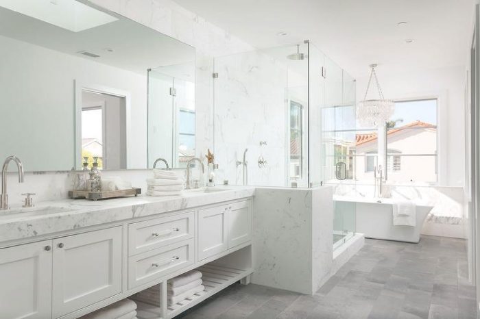 A bathroom with gray floors, marble counter tops, and a glass shower.