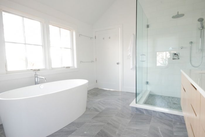 A modern bathroom with a white tub and glass shower featuring gray floors.