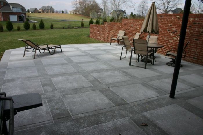 A gray concrete patio with chairs and a brick wall.