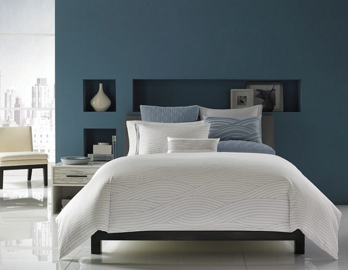 A bedroom with denim blue walls and white bedding.