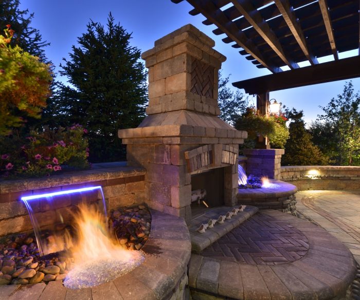 A modern stone fire pit in a backyard at dusk.