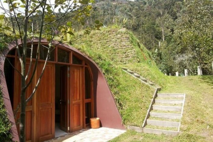 A Hobbit home with a green roof nestled in the middle of a grassy hill.