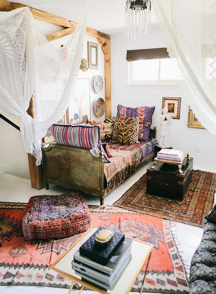 A bohemian living room with layered textures and a canopy over a bed.
