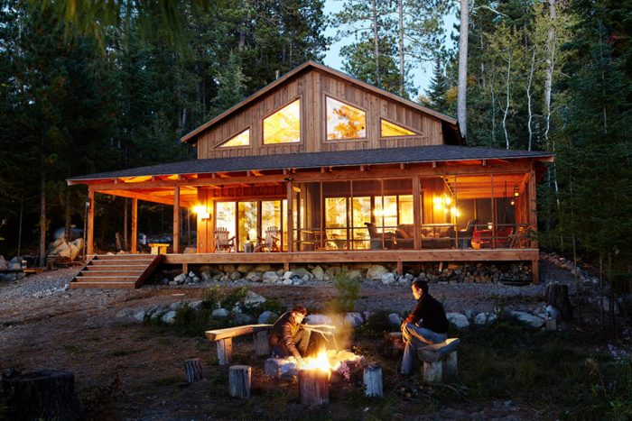 Two people sitting around a fire pit in front of a log cabin.