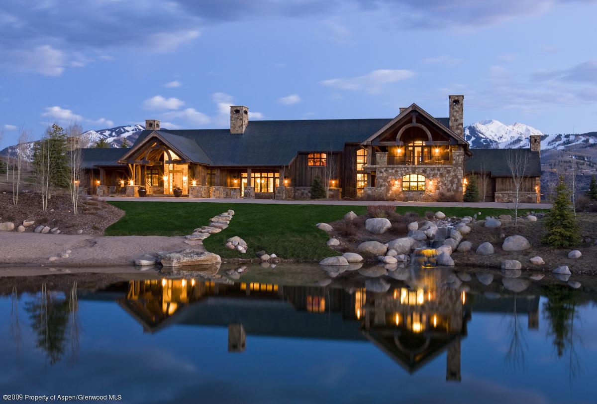 A large log cabin with a pond and mountains in the background.