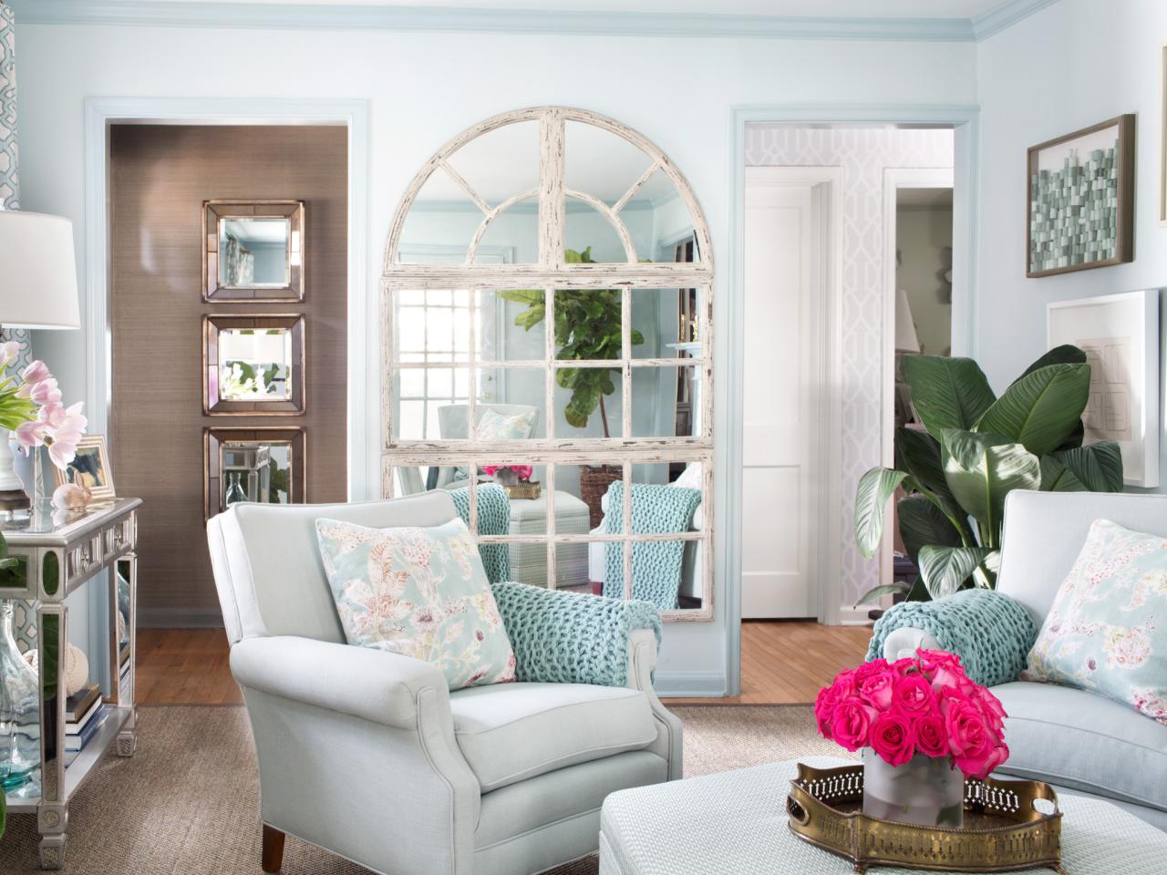 A living room with blue walls, white furniture, and mirrors for added visual depth.