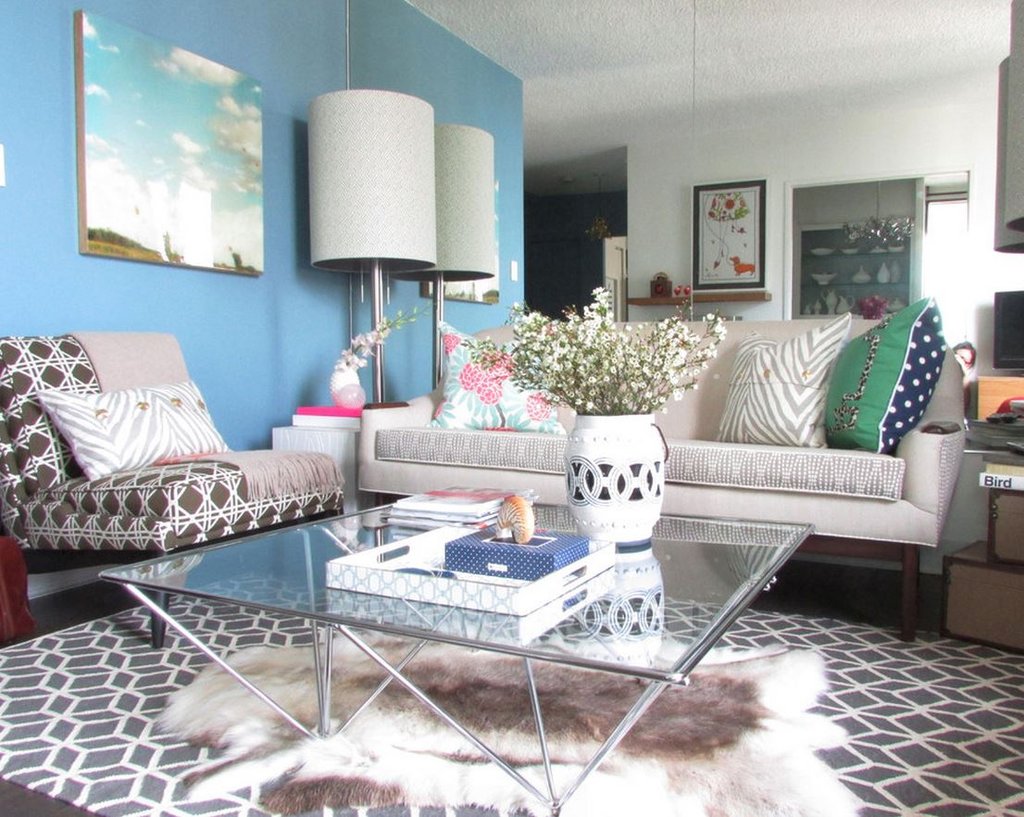 A living room with blue walls and white furniture featuring mixing patterns.