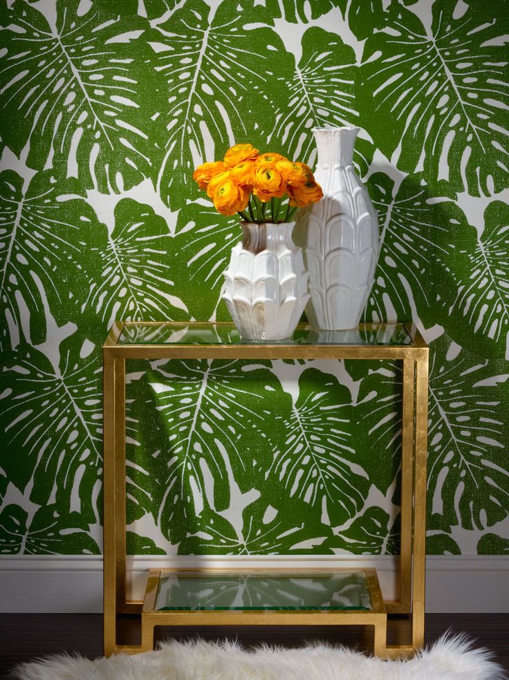 A table with a gold vase and tropical green leaves in front of it.