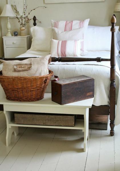 A white bedroom with a wooden bed and wicker basket in a pleasingly rustic farmhouse style.