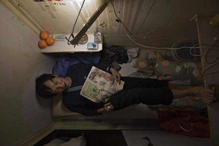 A man reading a newspaper in an unbelievably cramped room.
