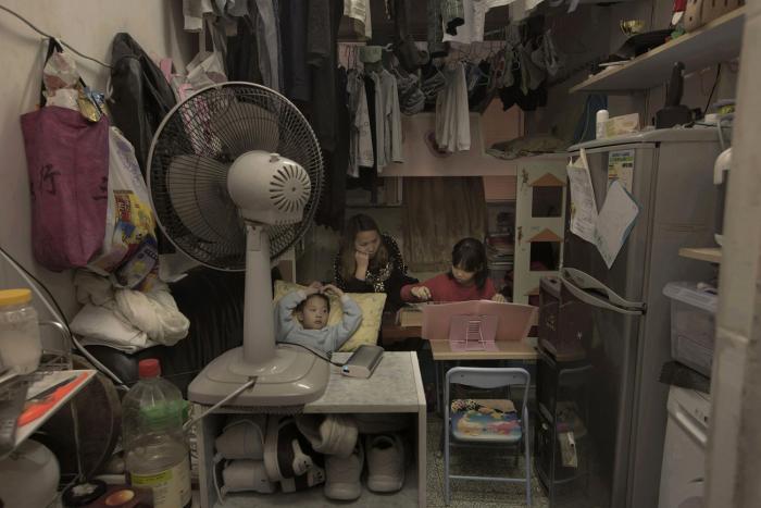 A woman is sitting in a cramped room with a laptop, revealing the unbelievable life inside Hong Kong's 'coffin homes'.