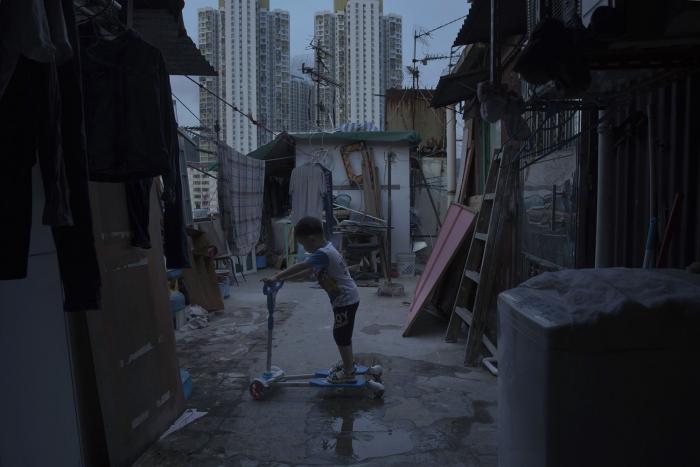 A boy riding a scooter in an alley, showcasing the unbelievable life inside Hong Kong's 'coffin homes'.