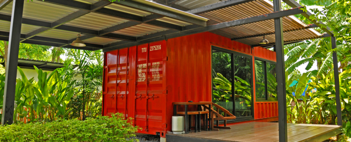 A tiny red container house sitting on a wooden deck.