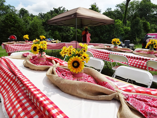 A table set up with sunflowers and red and white checkered tablecloths for backyard cookout decor.