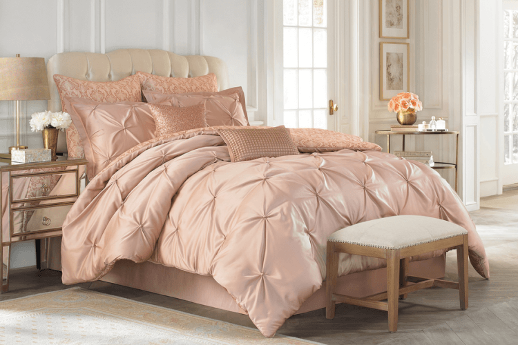 A pink comforter set with gold accents in a bedroom.