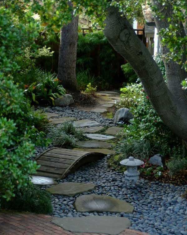 A stone pathway leads to a garden with trees and rocks, showcasing a beautiful rock garden.