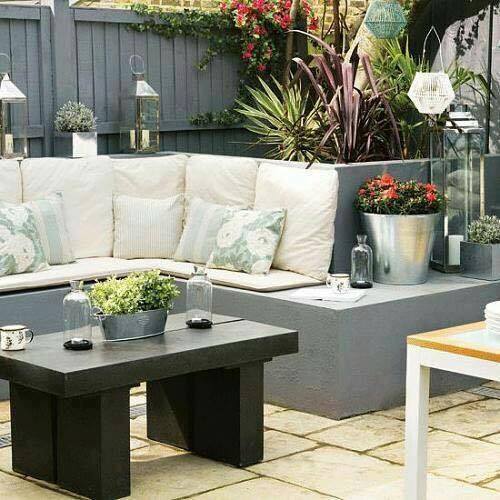 A backyard with a grey couch, table, and potted plants.
