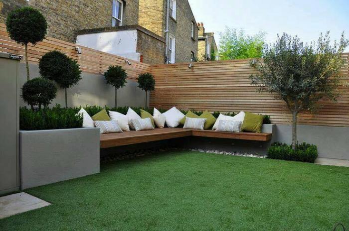 A small backyard garden with a wooden bench and green grass.
