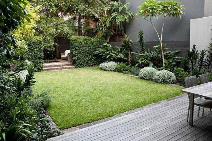 A small backyard garden with a wooden deck and green grass.