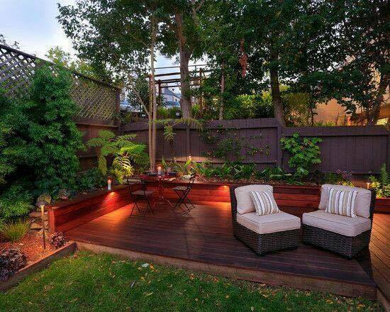 A small backyard garden with a wooden deck and lighting.