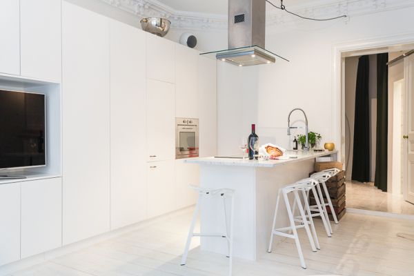 A white Swedish kitchen with stools and a TV.