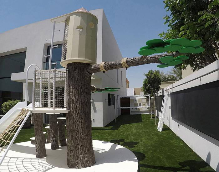 A Thinkterior with a Creative Contemporary Play area featuring a tree house and slide in front of a house.