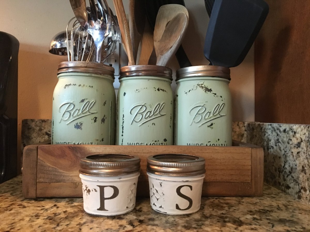 Three mason jars with utensils on a counter.