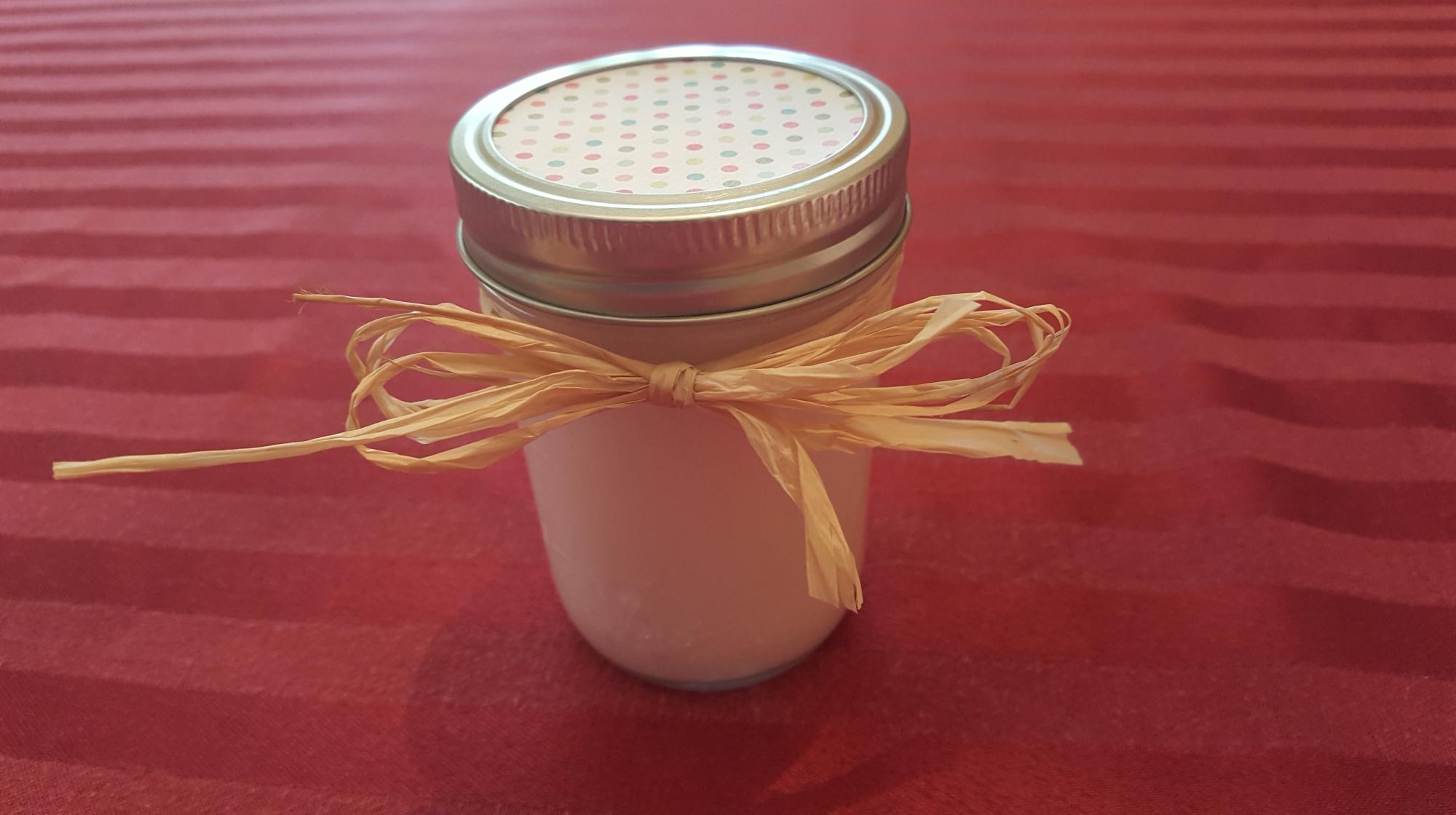 A small mason jar of lotion with a ribbon tied around it.