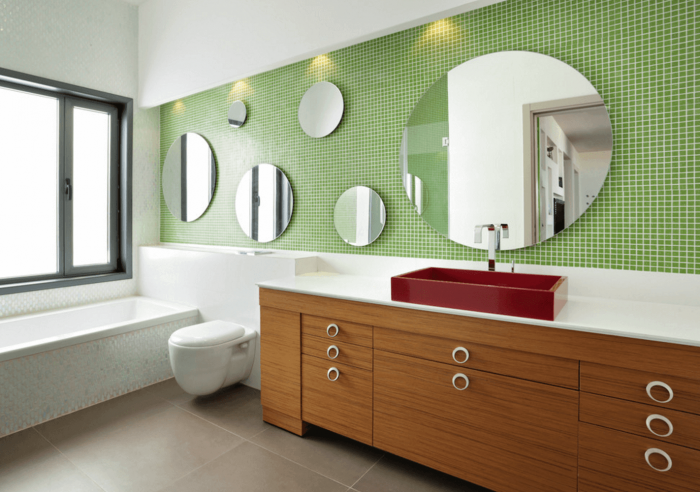 A bathroom with a green tiled wall and a bathroom mirror.