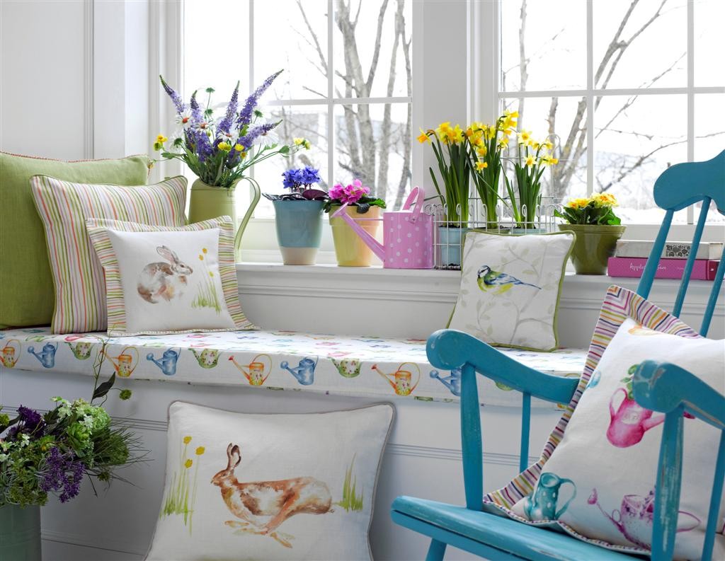 A blue rocking chair with pillows and Easter flowers in the window.
