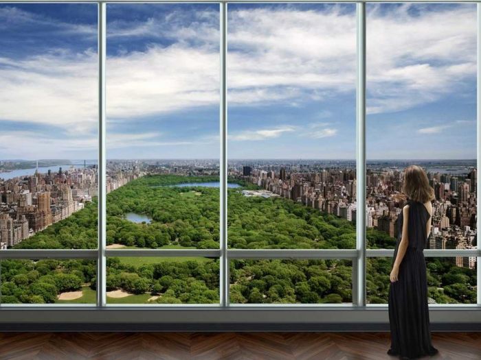 A woman in a penthouse apartment looking out of a window at a view of Central Park in New York City.