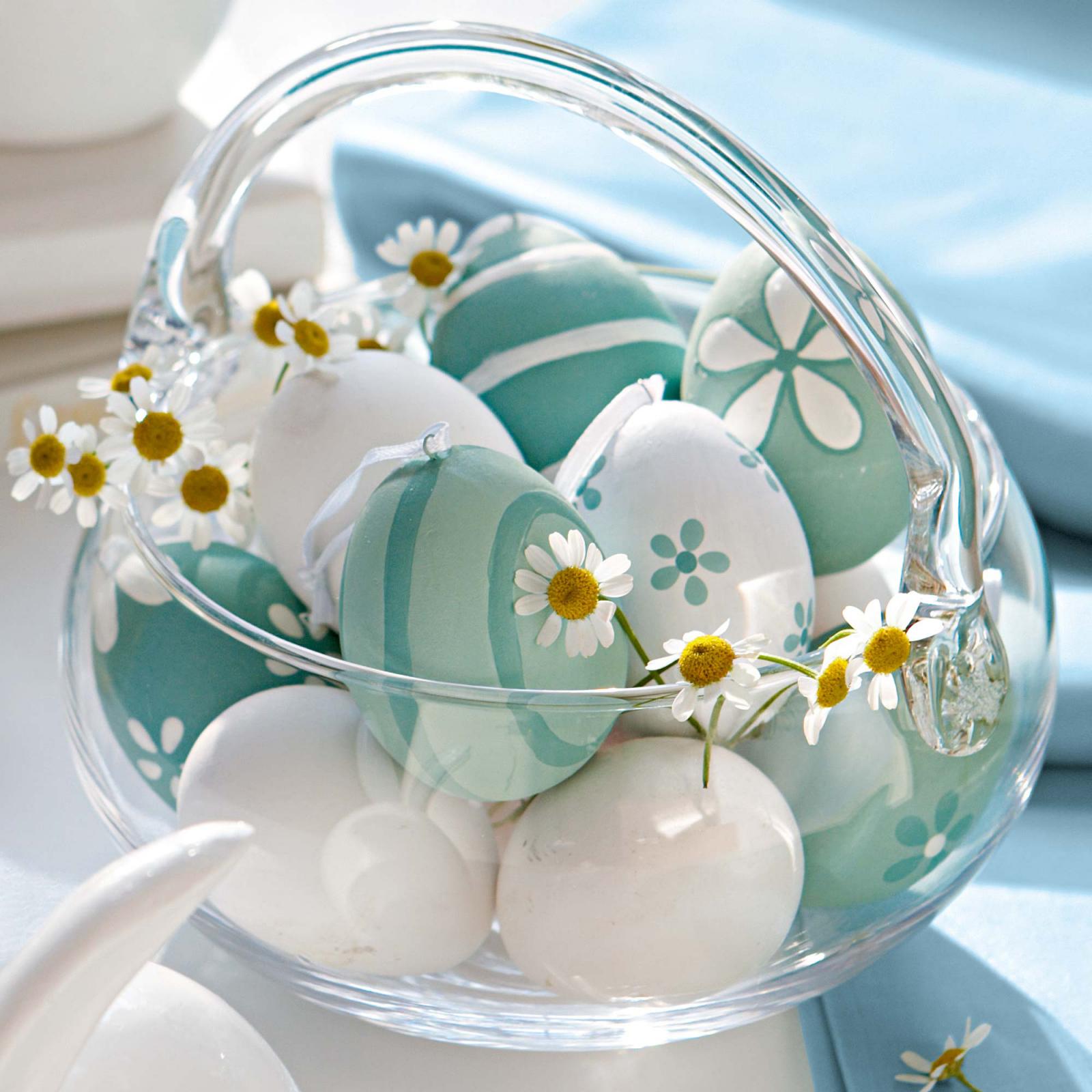 A glass bowl filled with Easter eggs and daisies.