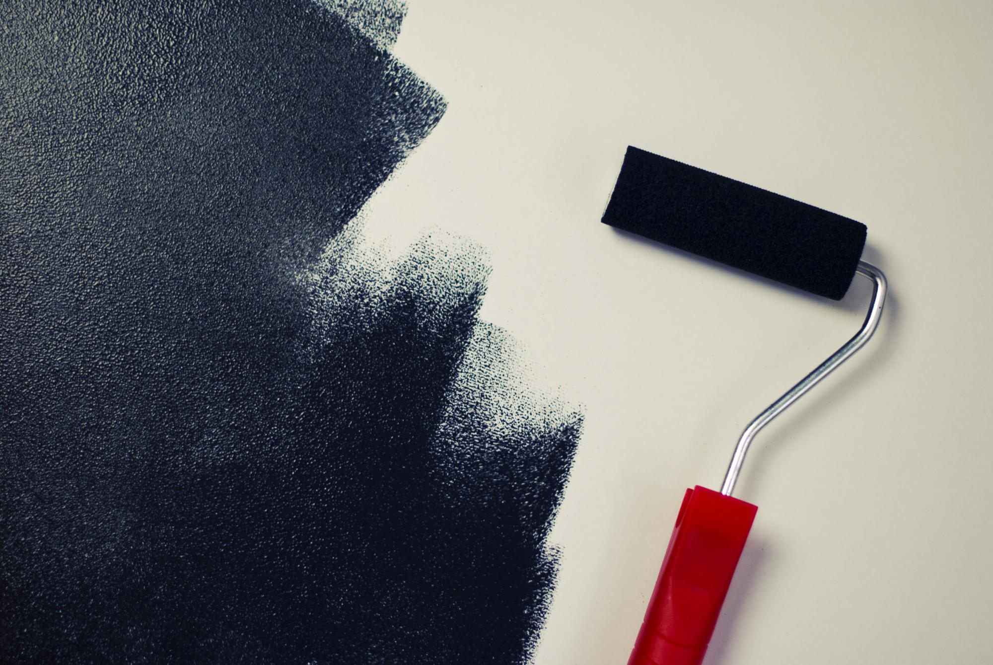A paint roller adding black paint on a white wall, demonstrating one of the 7 deadly sins of home decorating.