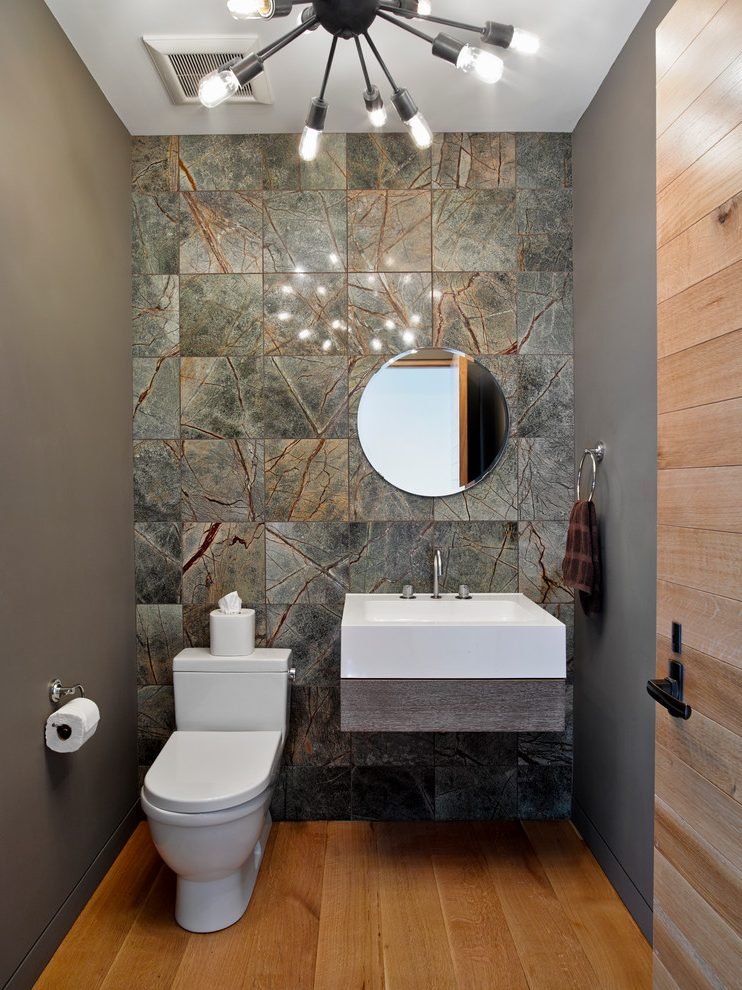 A modern tiny powder room with wood floors and tiled walls.