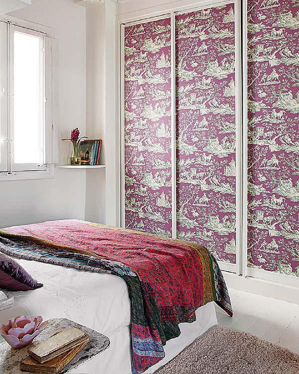 A bedroom with a bed and a bedside table featuring leftover wallpaper.
