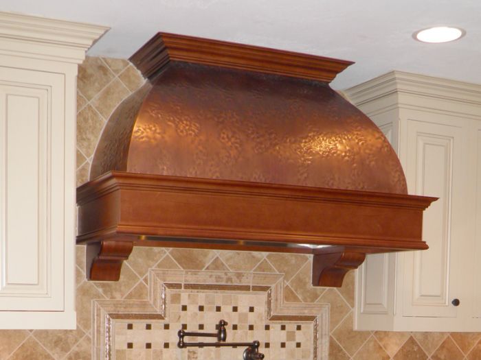 A copper kitchen with a hood over a sink.